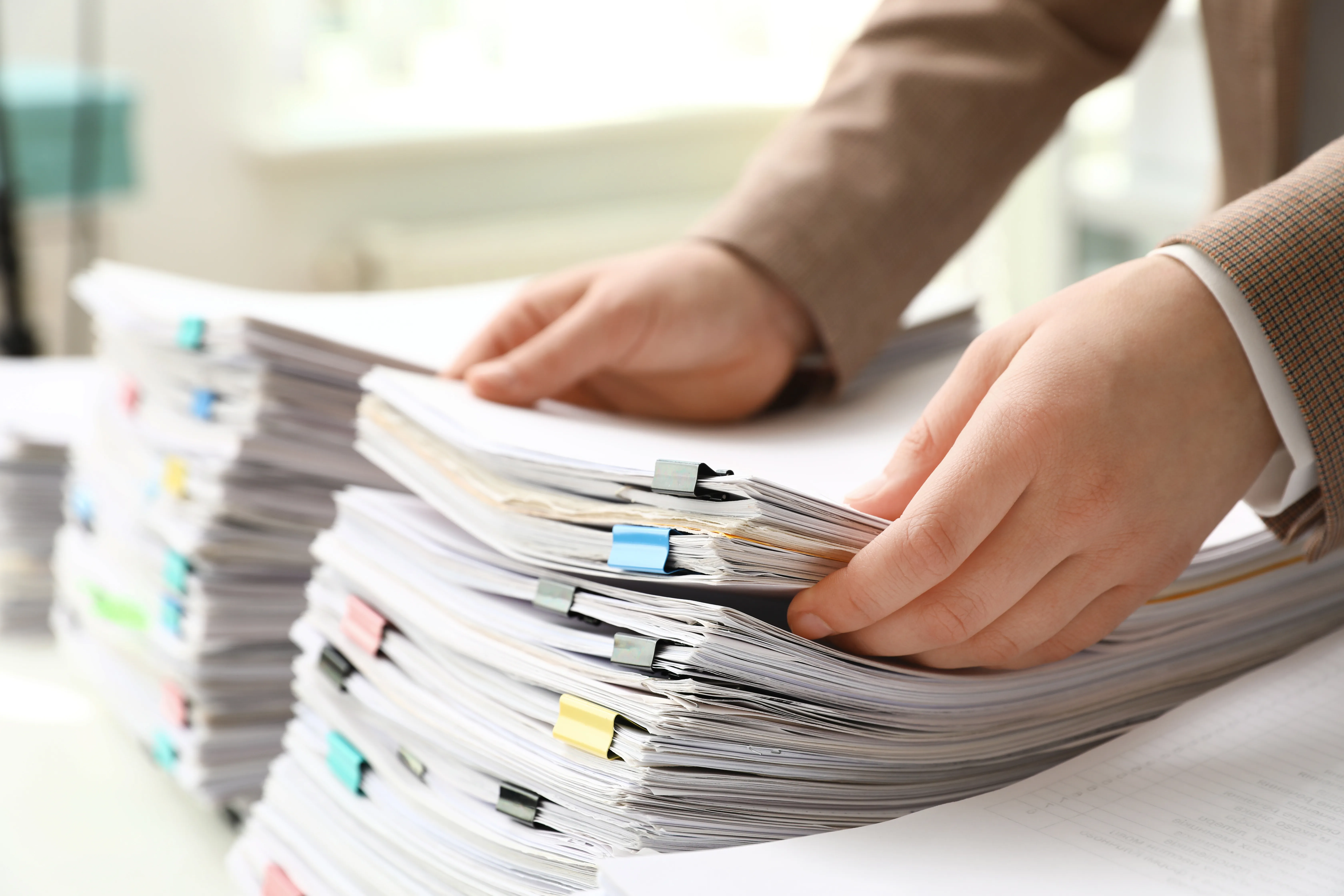Mani che sfogliano pile di documenti di gara con fermagli colorati