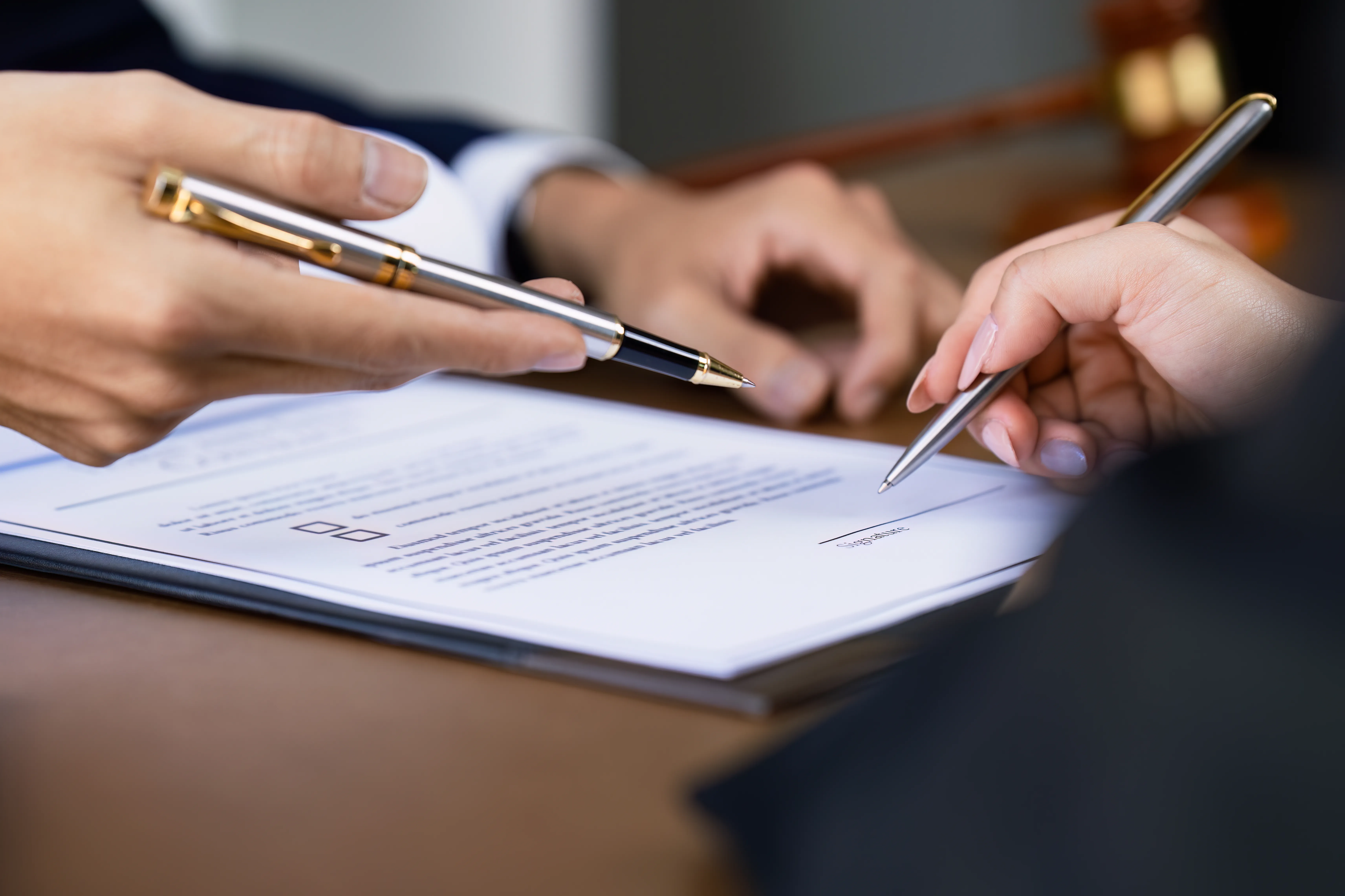 Mani che indicano con la penna il punto da firmare su un contratto
